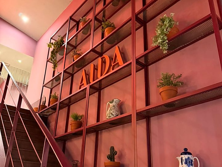 La escalera al primer piso, con un estante de hierro, plantas y las letras AIDA