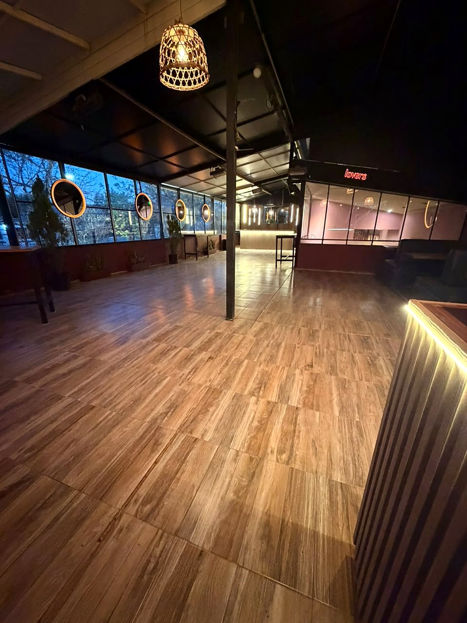 El salón de eventos de noche, con lámparas de mimbre y la barra al fondo